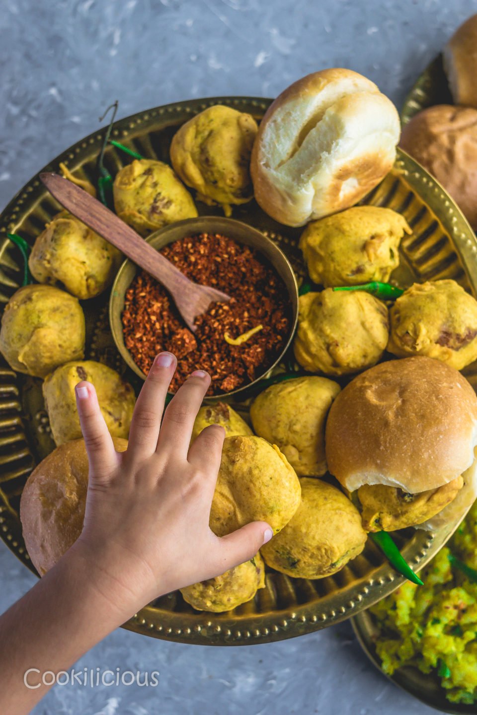 a child's hand reaching out to pick up a vada pav from a plate
