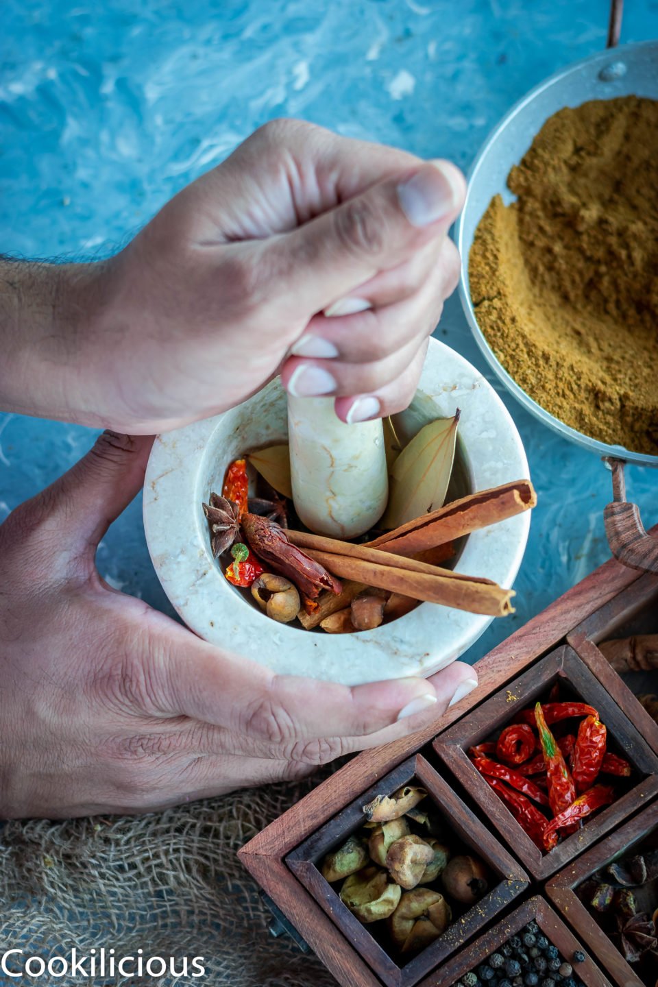 a set of hands working with a mortar and pestle to ground whole spices to make garam masala