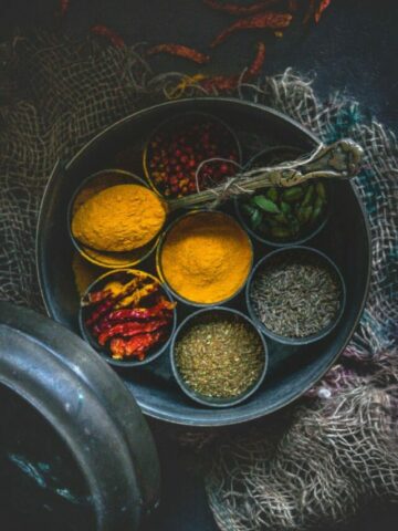 top angle shot of a masala box with compartments filled with different spices and one of them is filled with turmeric powder