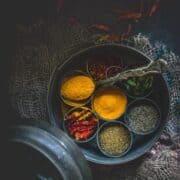 top angle shot of a masala box with compartments filled with different spices and one of them is filled with turmeric powder