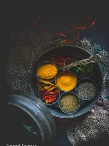 top angle shot of a masala box with compartments filled with different spices and one of them is filled with turmeric powder