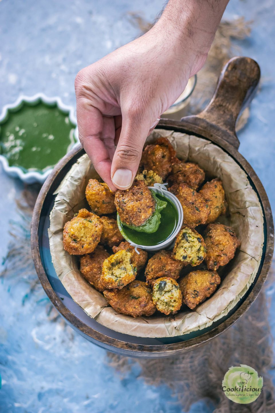 a hand dunking one Crispy Moong Dal Pakora (one of the popular easy vegan appetizers) into a bowl of green chutney