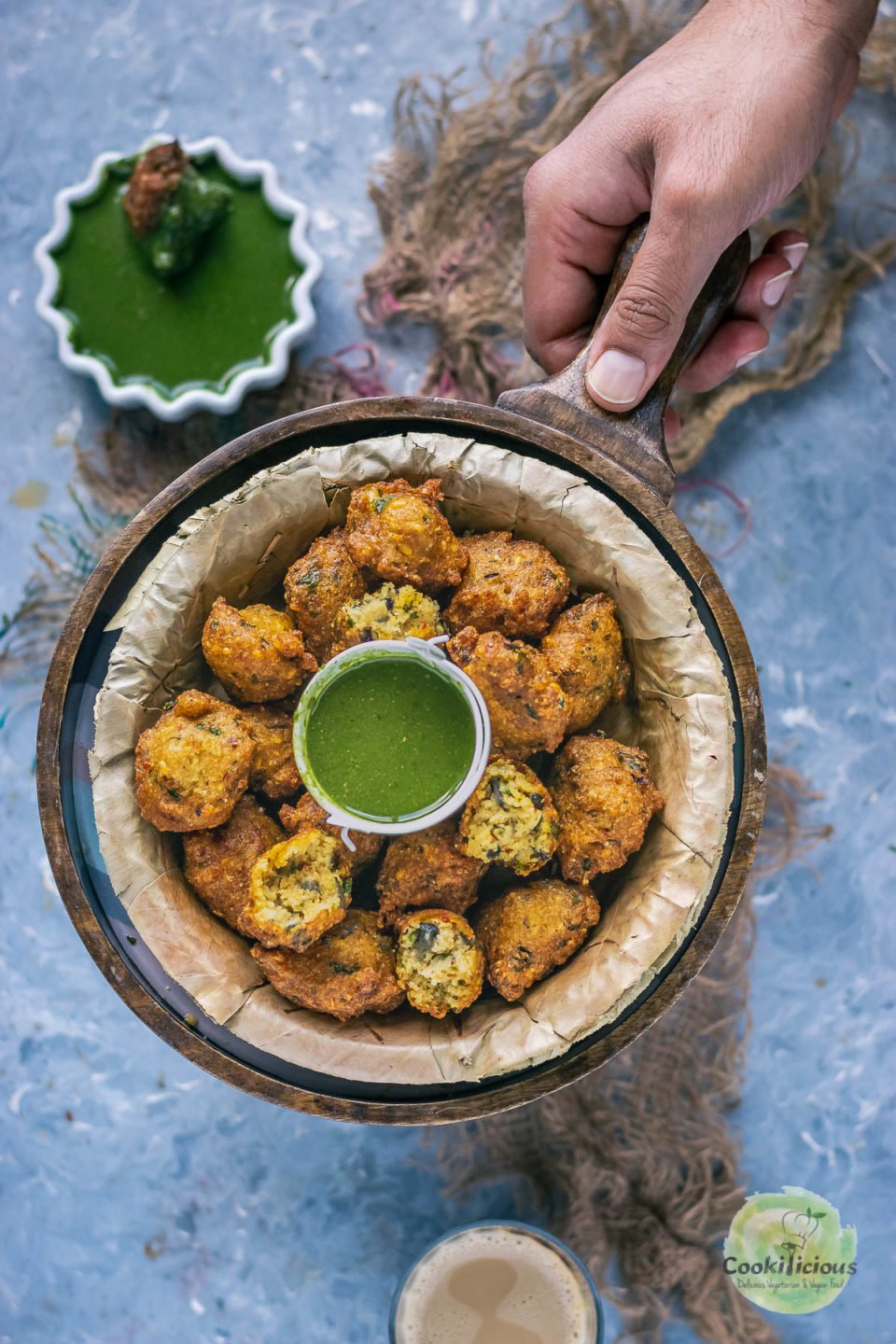 a hand holding a serving platter which has a bowl of Crispy Moong Dal Pakora (one of the popular easy vegan appetizers) and a bowl of green chutney next to it.