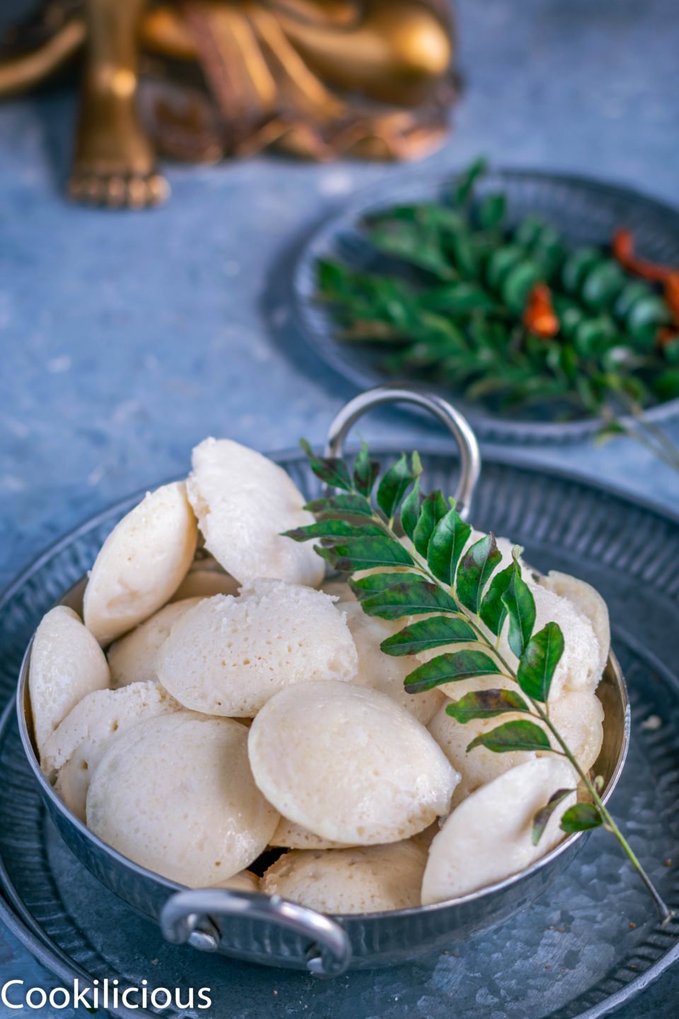 a bowl of Mini Masala Idli with a sprig of curry leaves on top
