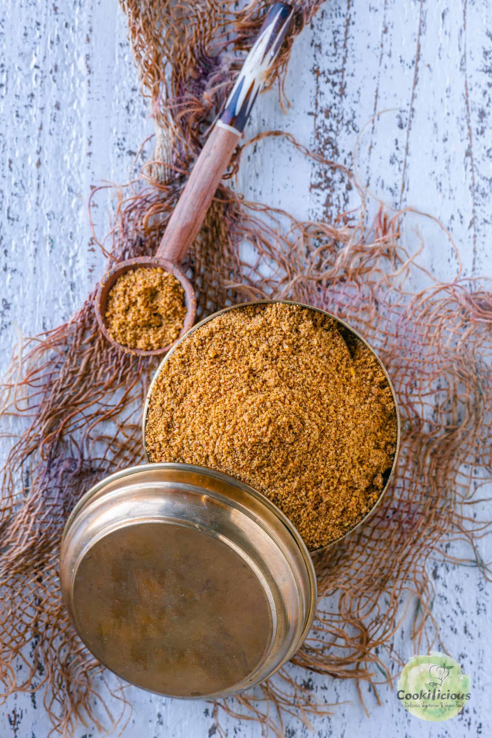 Dosa molaga podi served in a small brass dabba with a lid and spoon on the side.