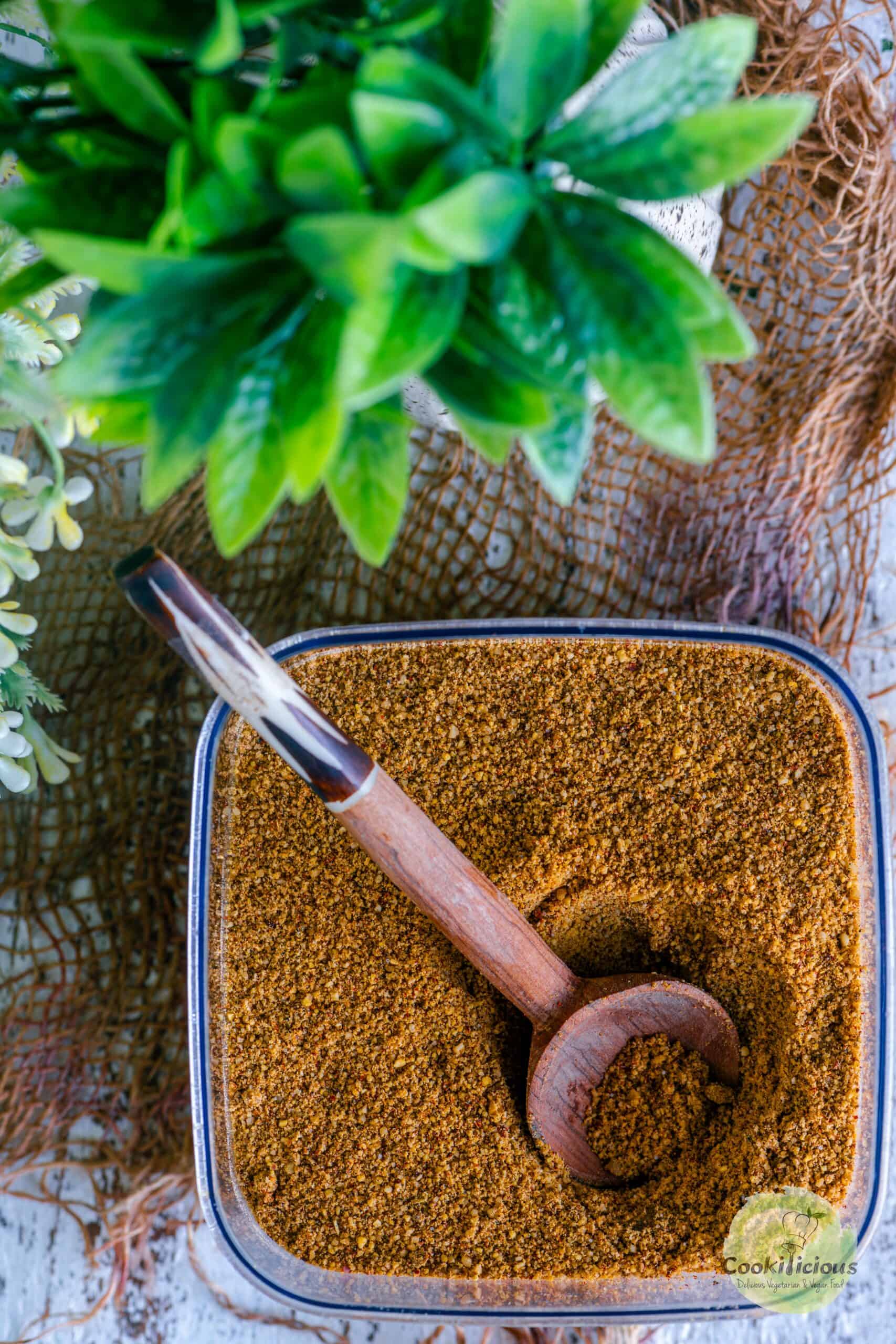 Top view of a container filled with idli milagai podi with a wooden spoon in it.