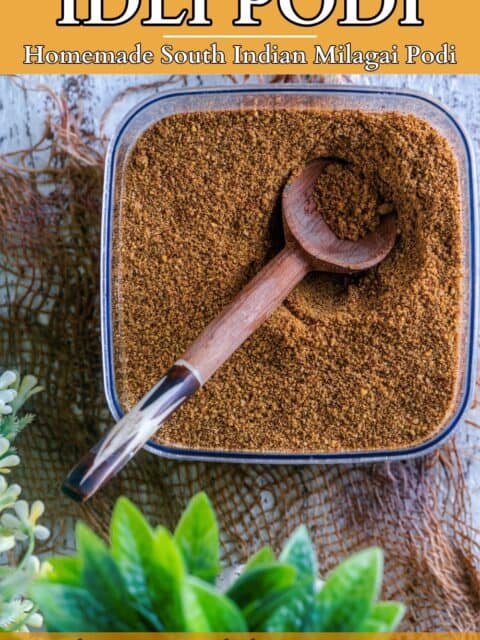 Top view of a container filled with idli milagai podi with a wooden spoon in it and text at the top and bottom.