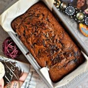 flat lay image of Eggless Chickoo Fig Loaf Cake in a loaf pan and a book on one side and a photo frame on the other side.