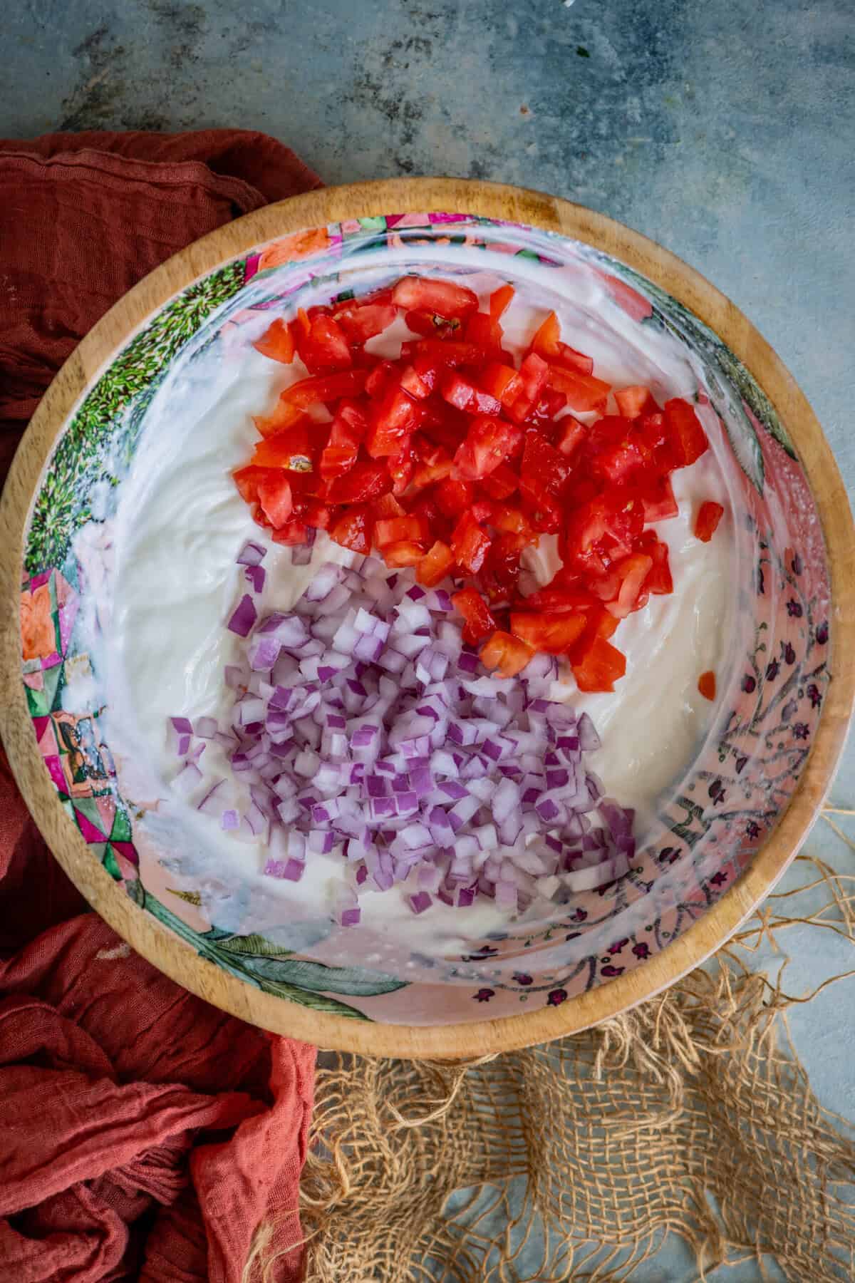 Chopped onions and tomatoes added to whisked yogurt for koshimbir recipe.