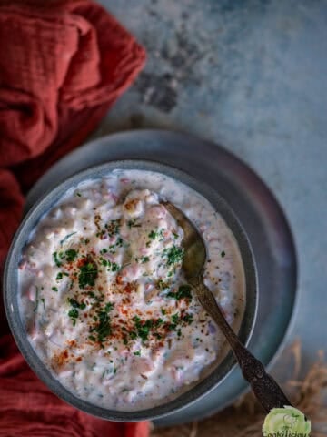 Close-up of koshimbir garnished with cilantro and red chili powder in a bowl with a spoon.