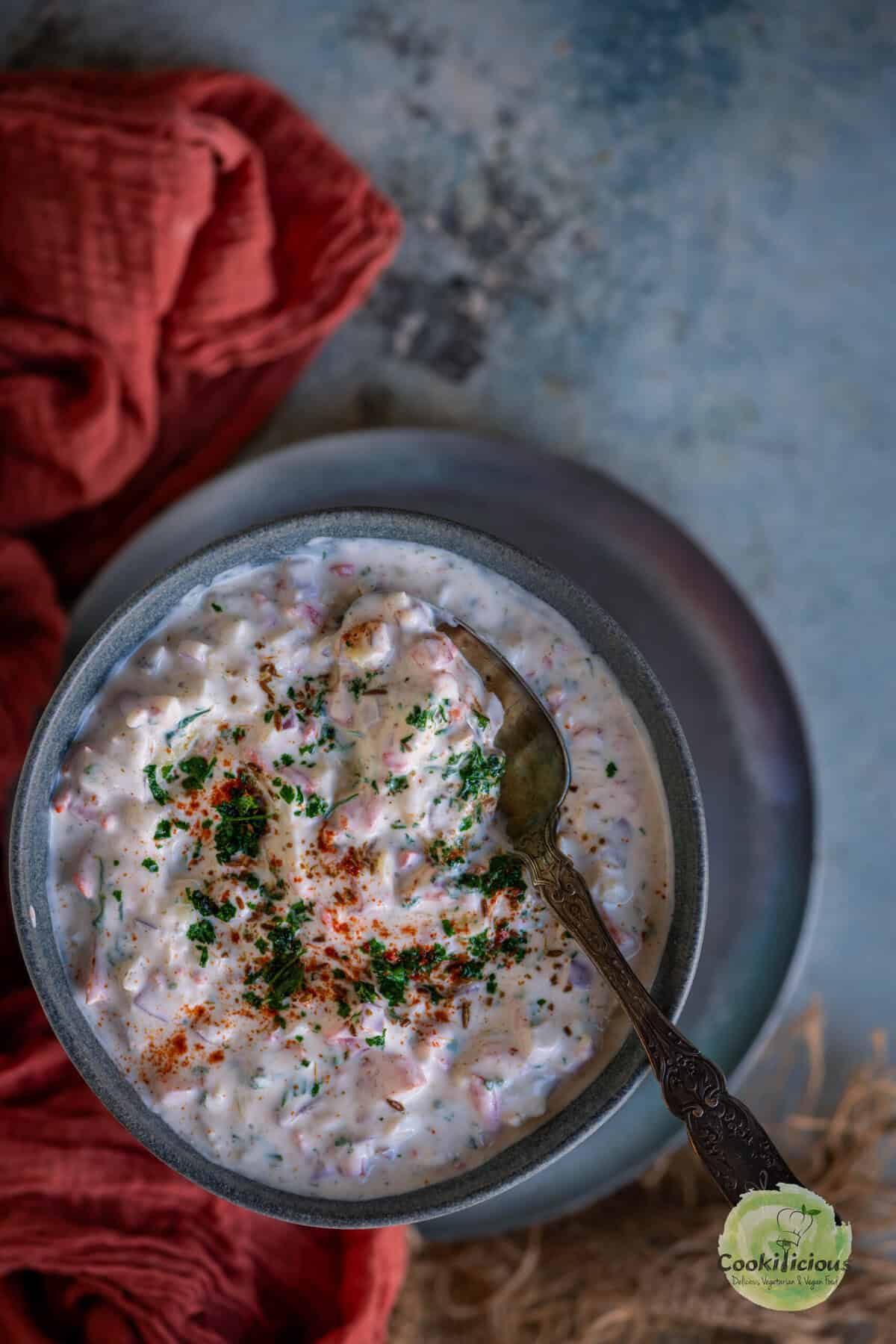 Close-up of koshimbir garnished with cilantro and red chili powder in a bowl with a spoon.