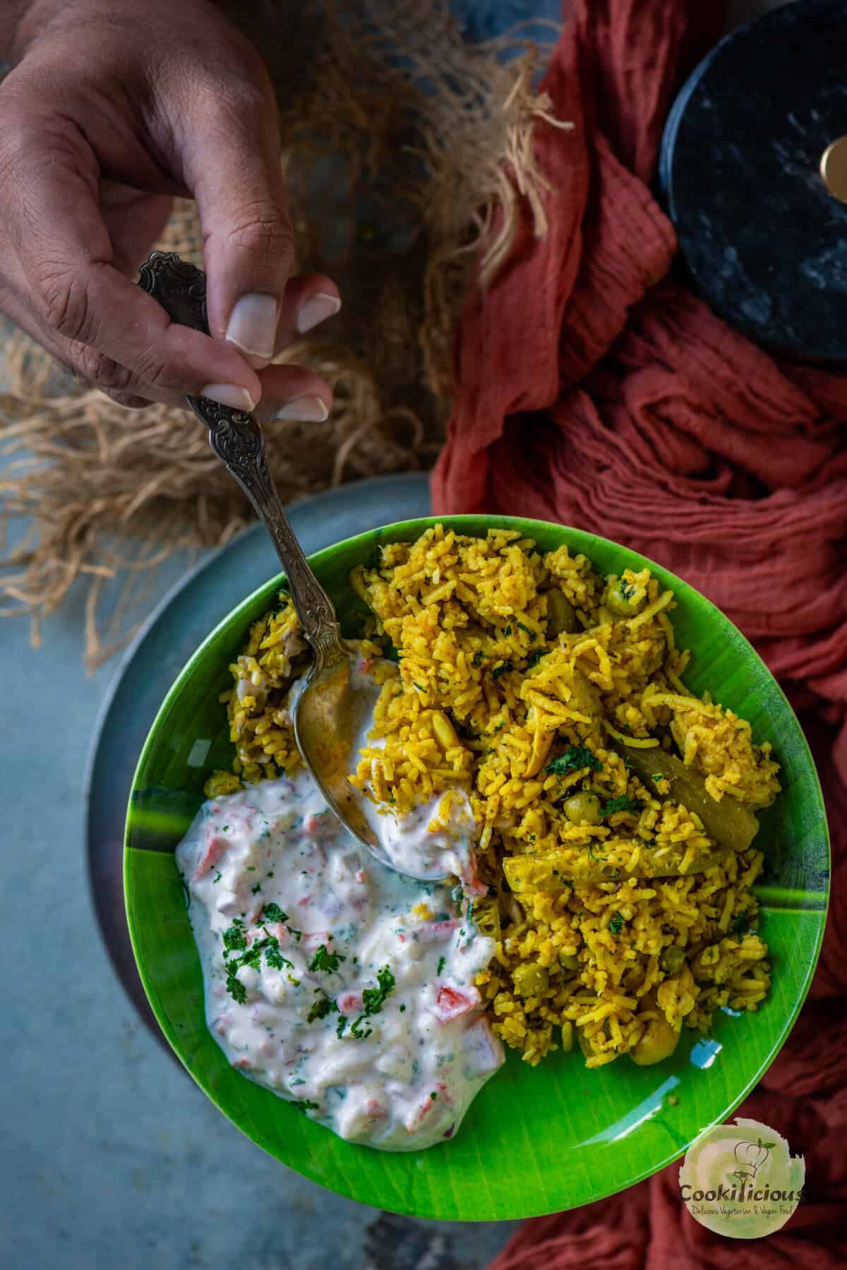 A hand holding a spoon over a banana leaf plate filled with koshimbir and masale bhat.