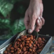 A hand using a scoop to get some Smoky Spicy Garlic Roasted Almonds from the platter