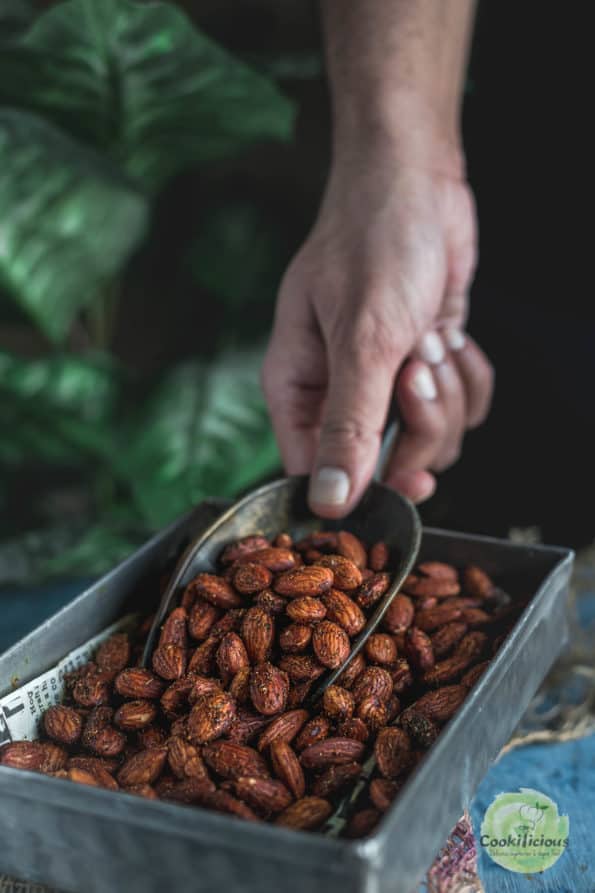 A hand using a scoop to get some Smoky Spicy Garlic Roasted Almonds from the platter