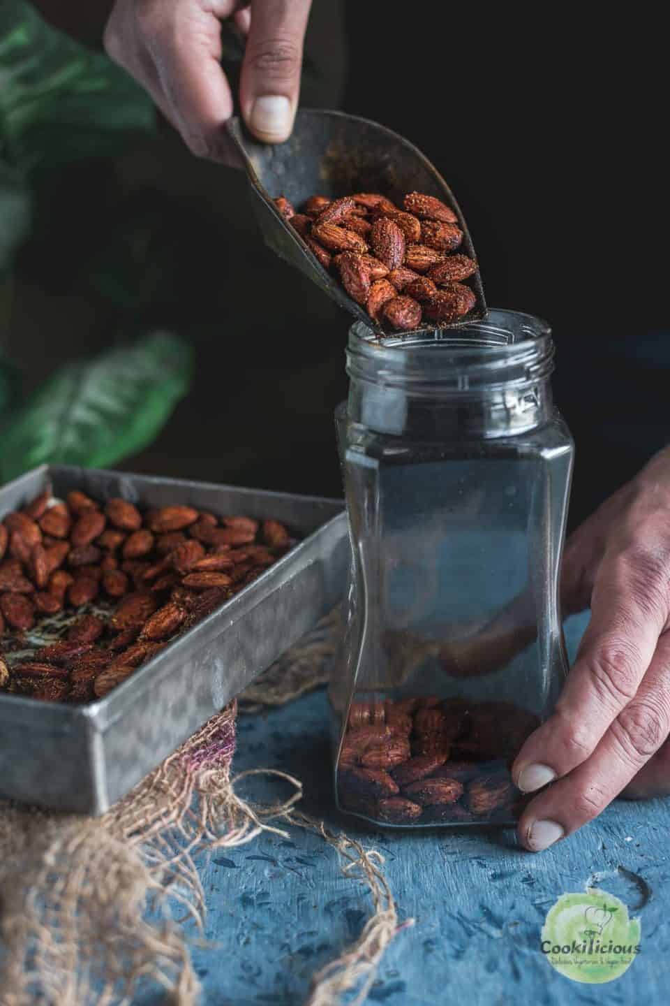 a hand pouring some Smoky Spicy Garlic Roasted Almonds into a glass jar