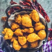 Flat lay shot of South Indian Medu Wada | Lentil Fritters in a kadai with dried red chillies around it.