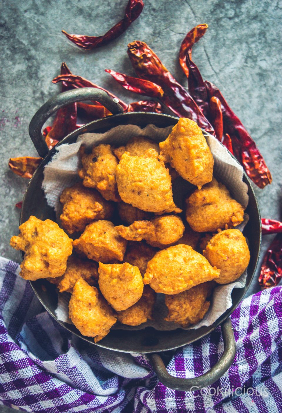 Flat lay shot of South Indian Medu Wada | Lentil Fritters in a kadai with dried red chillies around it.