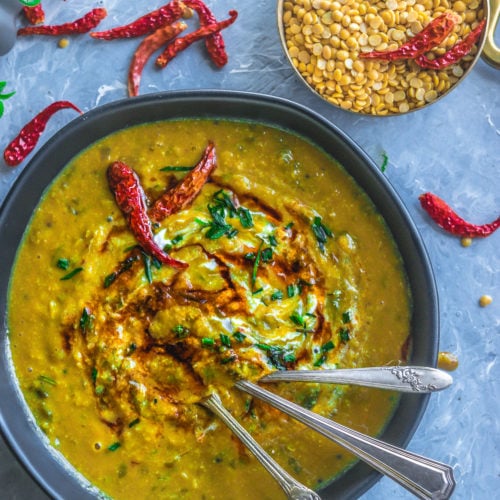 a ceramic bowl filled with Malvani Style Tikhat Dal with 3 spoons in it and a bowl of dry lentils besides it