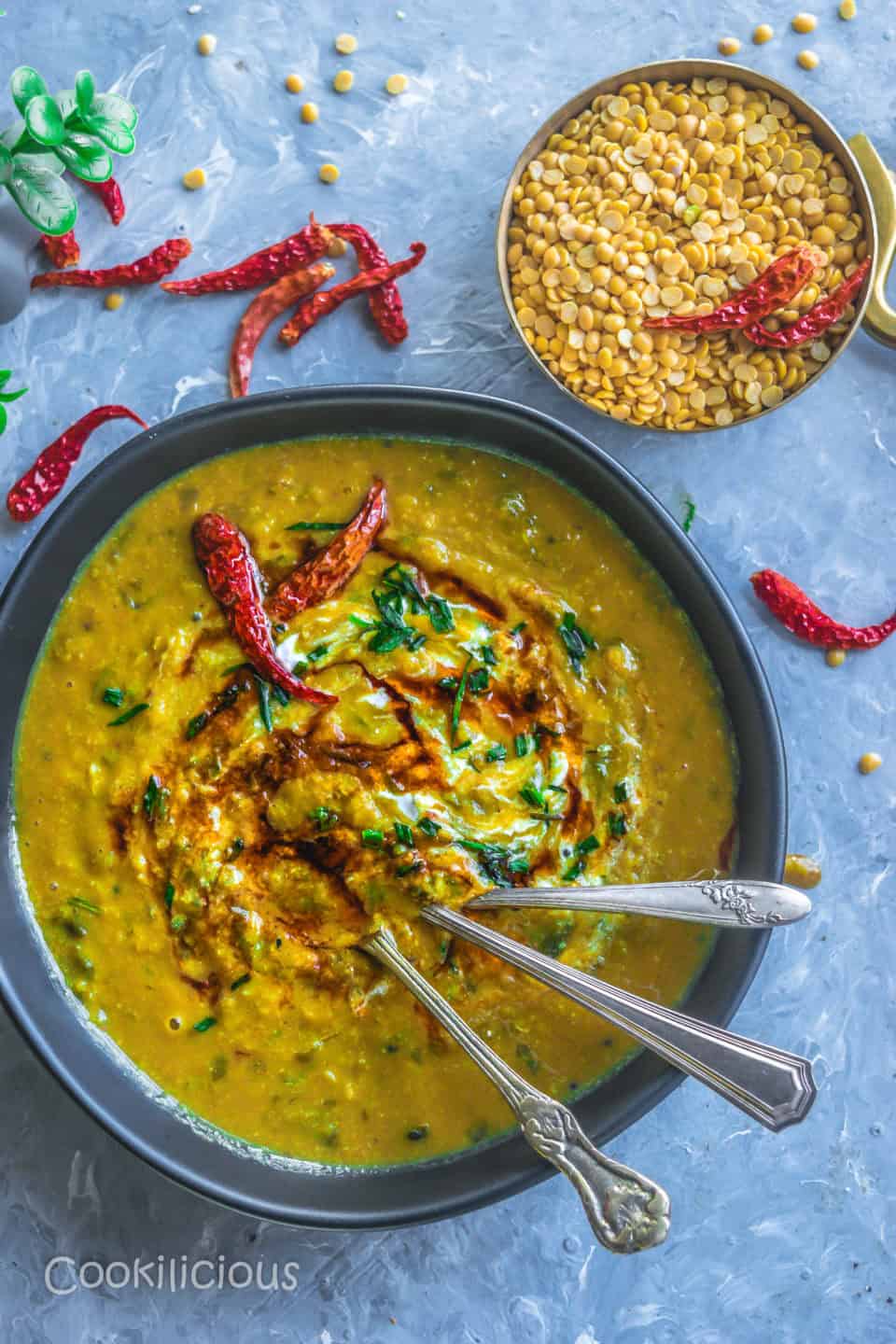 a ceramic bowl filled with Malvani Style Tikhat Dal with 3 spoons in it and a bowl of dry lentils besides it