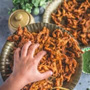 a child's hand reaching out to a plate filled with Vegan Crispy Onion Pakoda | Fried Kanda Bhajiya