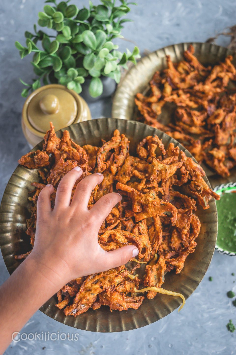 a child's hand reaching out to a plate filled with Vegan Crispy Onion Pakoda | Fried Kanda Bhajiya