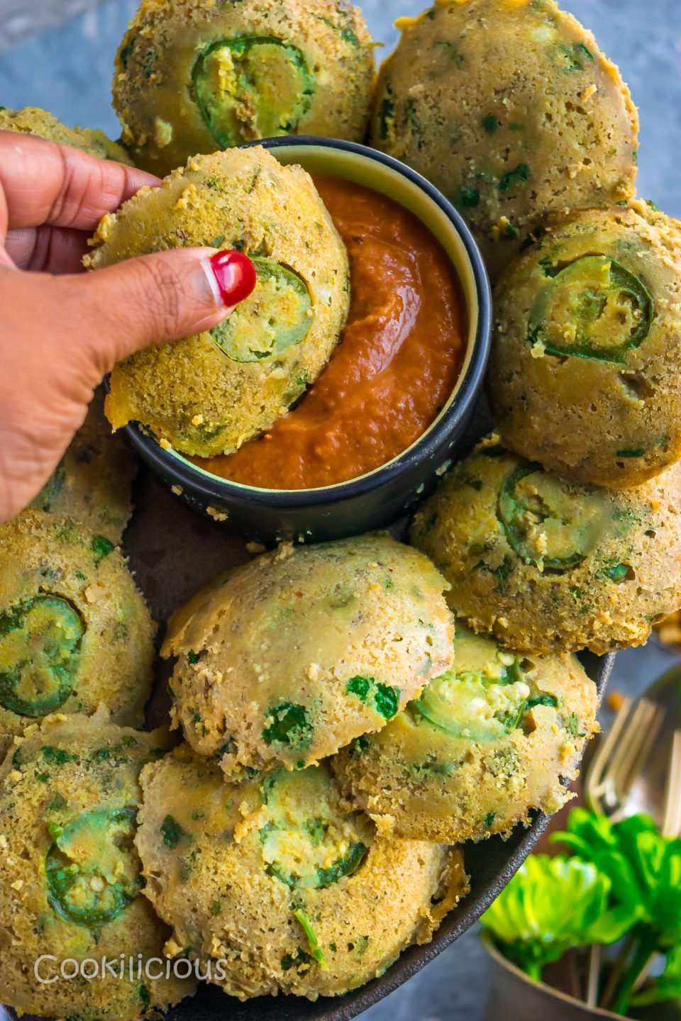 a hand holding one Steamed Chana Dal Lentil Bafauri and dipping it into a bowl of tomato chutney