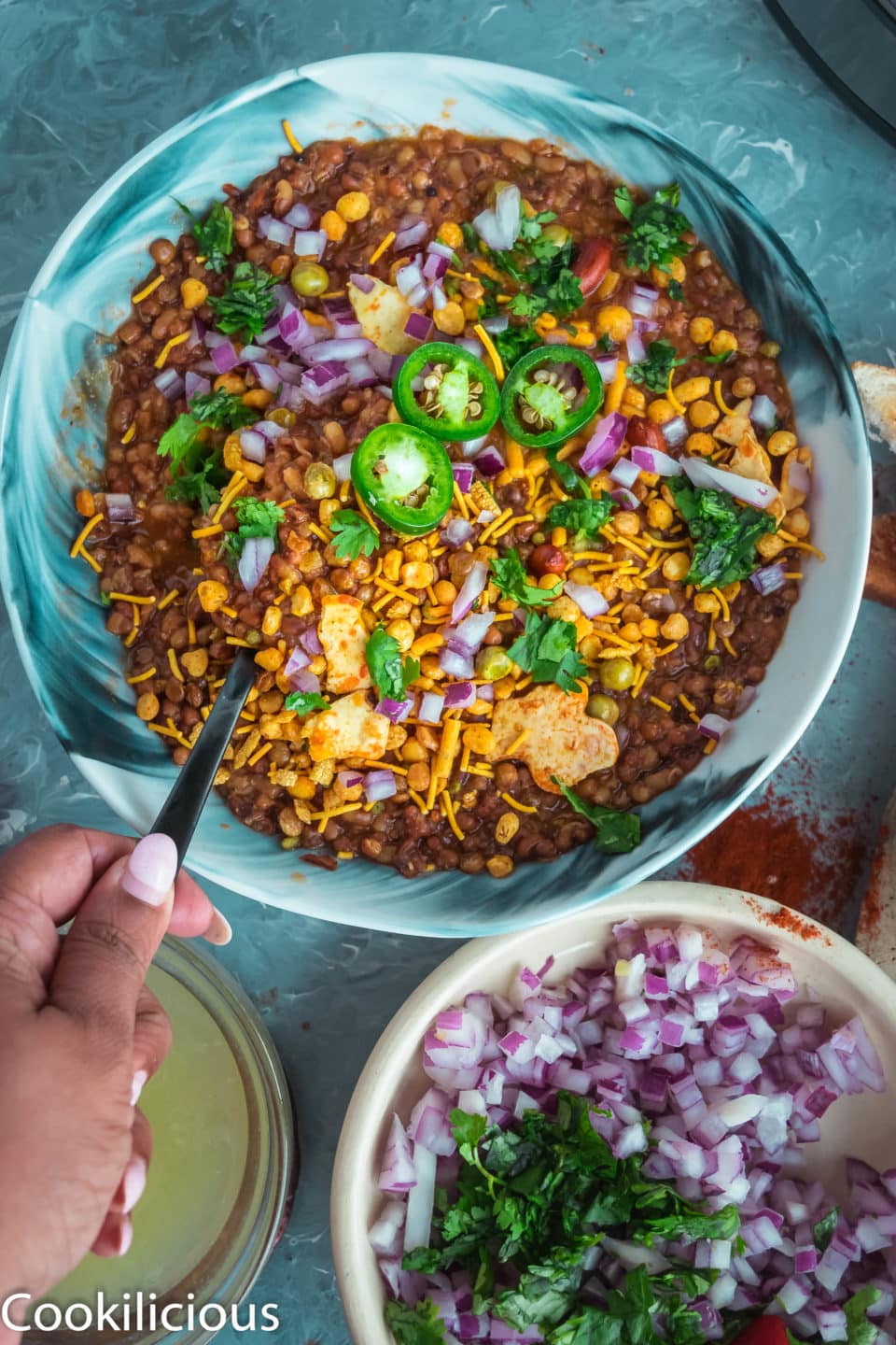 a handing holding a spoon and digging into a bowl of Vegan Matki Misal