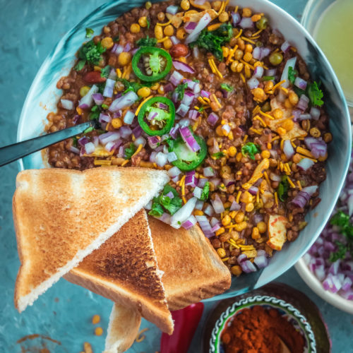 top angle close up shot of a bowl filled with Vegan Matki Misal with bread slices around it