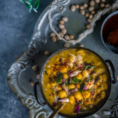 Instant Pot Potato Chickpeas Vegan Curry served in a bowl with a spoon in it placed over a tray