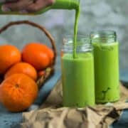 a hand holding a bottle and pouring Super Healthy Mango Spinach Yogurt Power Smoothie into a glass