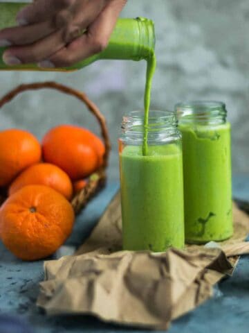 a hand holding a bottle and pouring Super Healthy Mango Spinach Yogurt Power Smoothie into a glass