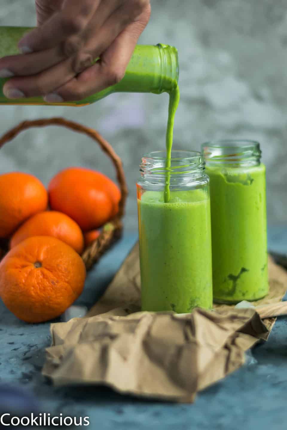 a hand holding a bottle and pouring Super Healthy Mango Spinach Yogurt Power Smoothie into a glass