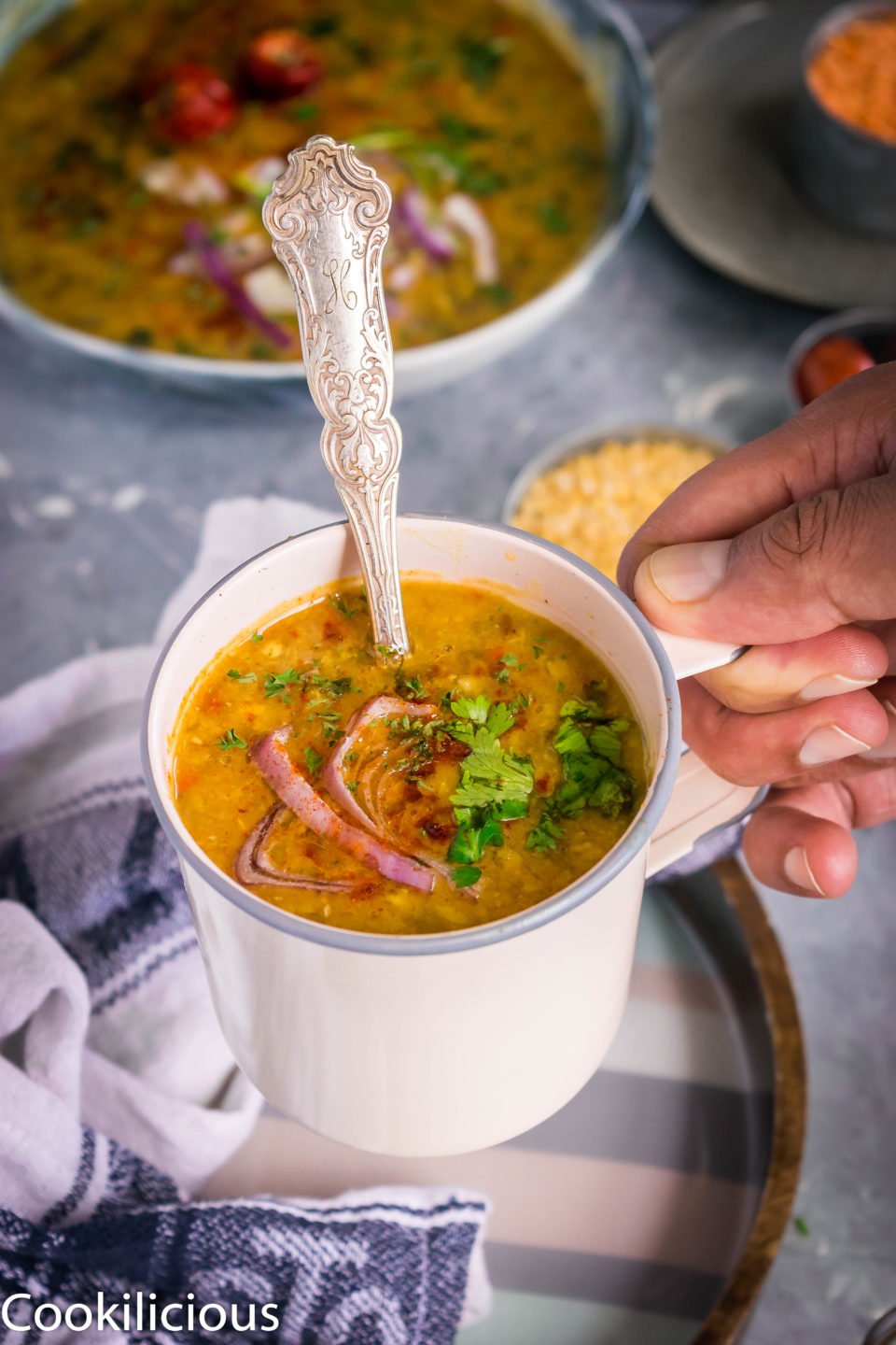 close up shot of a hand lifting a mug filled with Indian Style Green Moong Sprouts Dal Fry 