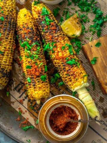 2 Indian Street Style Corn On The Cob on a platter with a bowl of spice rub on the side