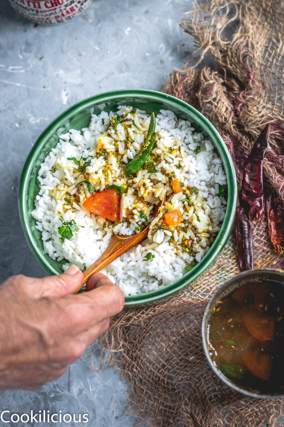 a hand mixing South Indian Tomato Rasam With Pink Lentils with rice in a bowl with a spoon