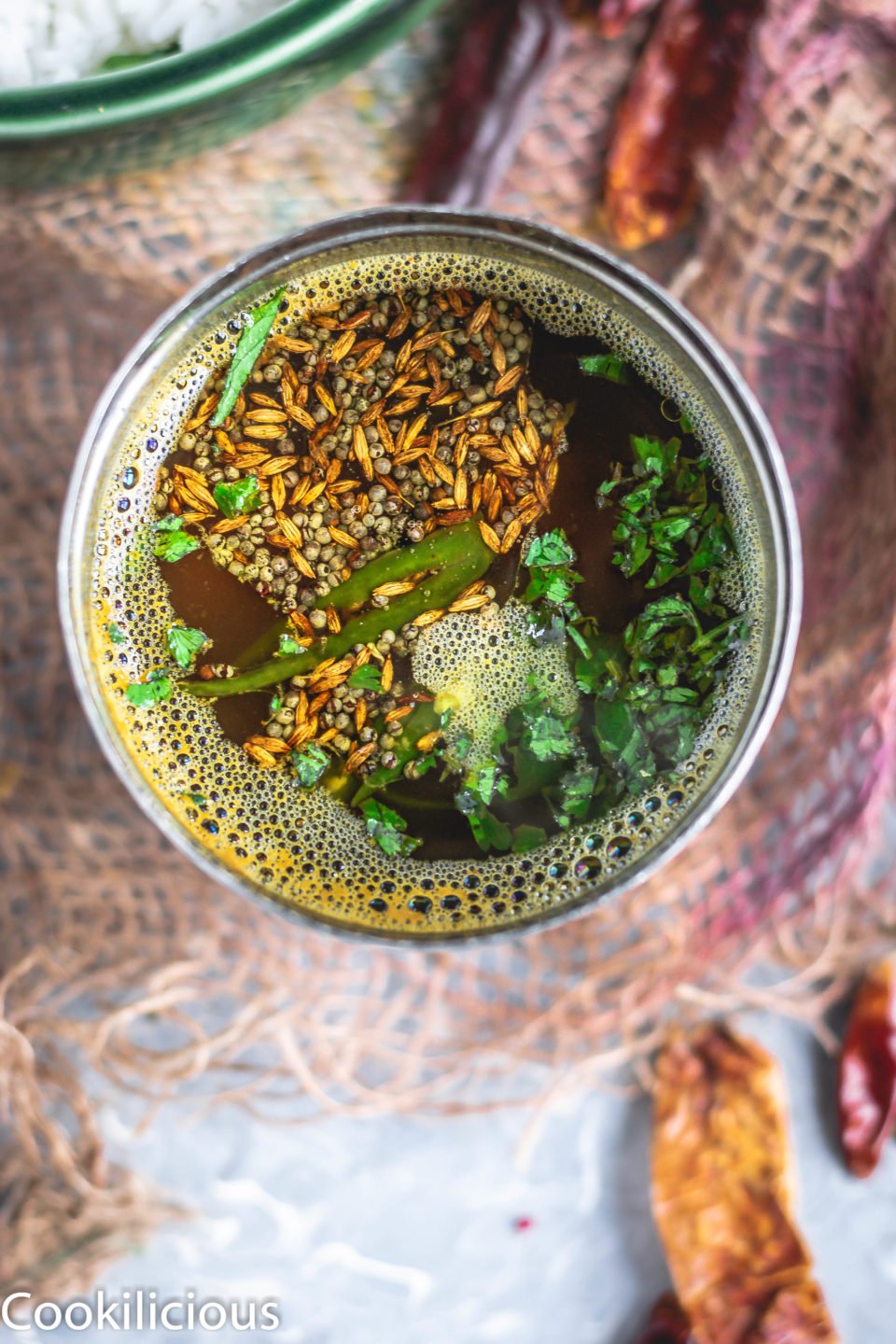 top angle shot of South Indian Tomato Rasam With Pink Lentils in a steel vessel with tadka on top