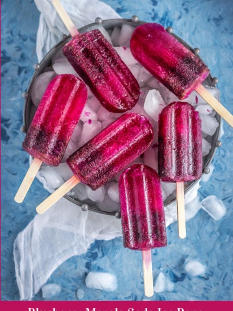 many Masala Soda Blueberry Popsicles placed on a tray filled with ice cubes and text at the bottom