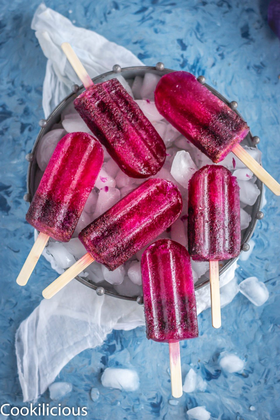 many Masala Soda Blueberry Popsicles placed on a tray filled with ice cubes