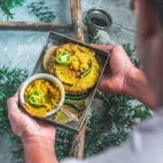 a man holding a square tray filled with Bajra Jowar Bhakhri and zunka