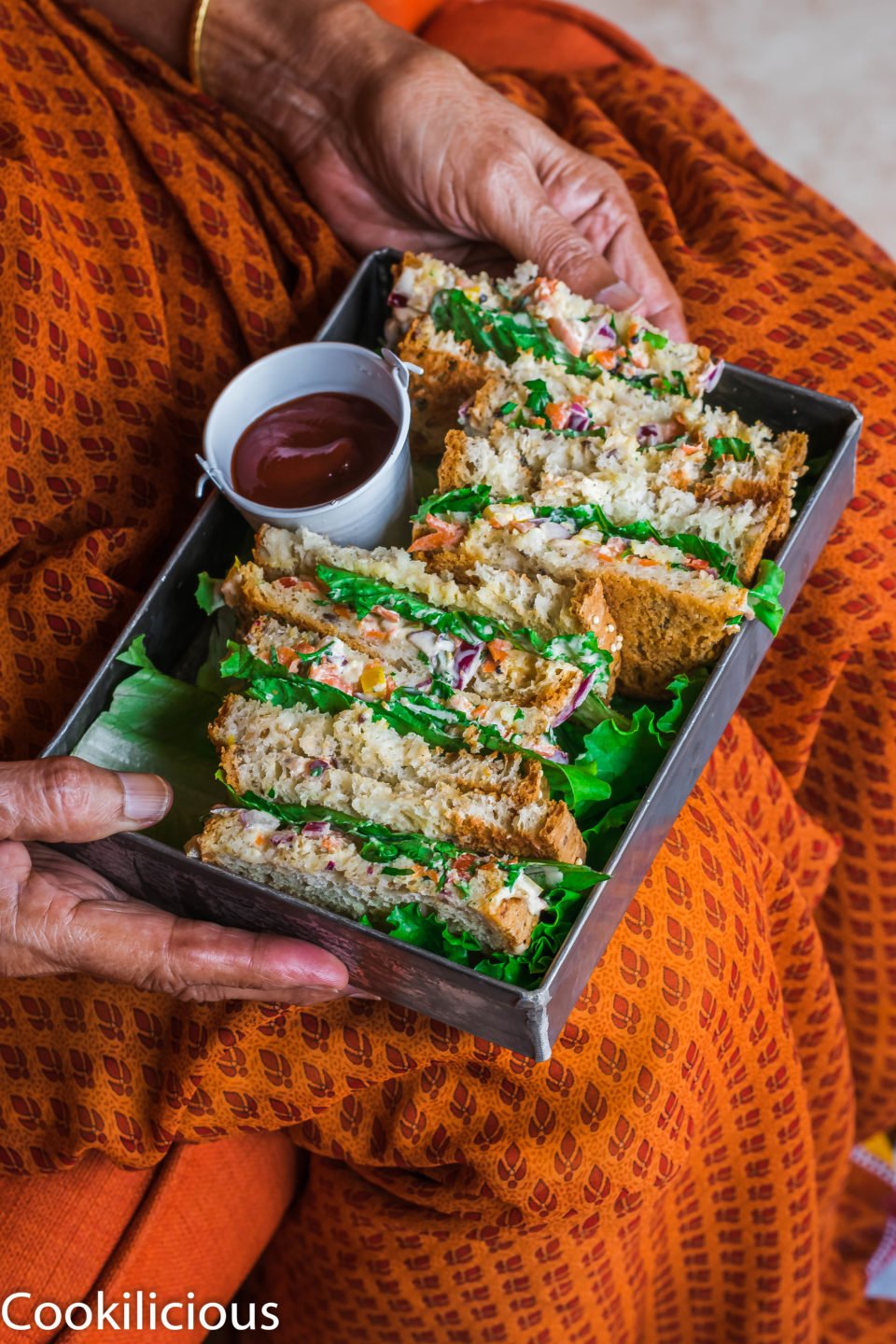 a tray filled with Indian Style Spiced Yogurt Sandwiches resting on the lap of a woman