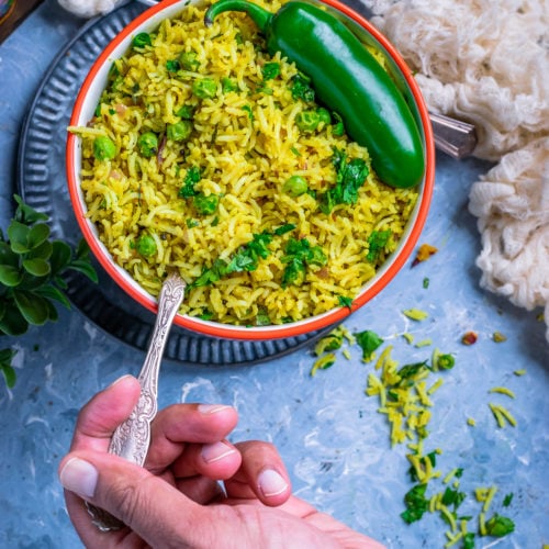 a hand holding a spoon and digging into a bowl of Green Peas Pulao