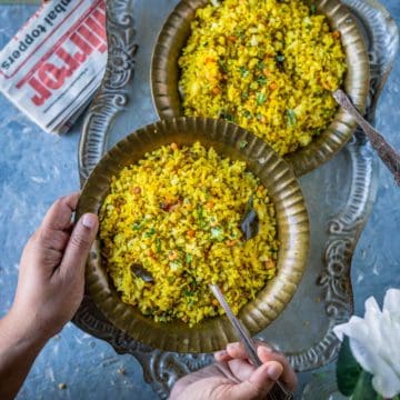 a set of hands holding a plate of tamarind poha