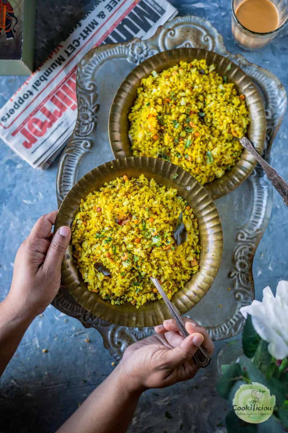 a set of hands holding a plate of tamarind poha