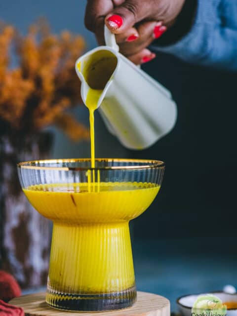 A hand pouring golden milk in a glass.