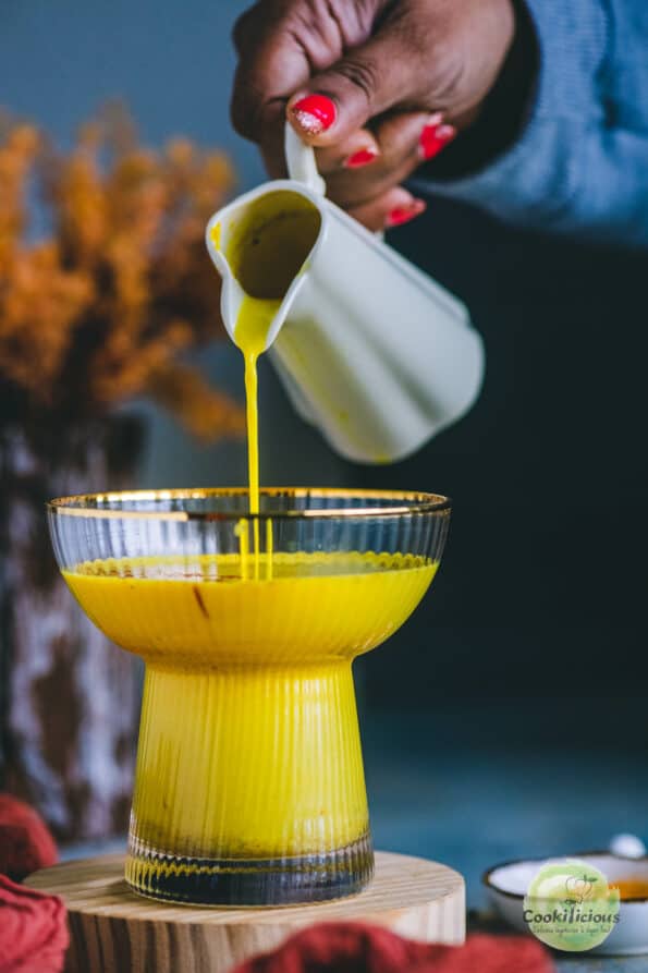 A hand pouring golden milk in a glass.