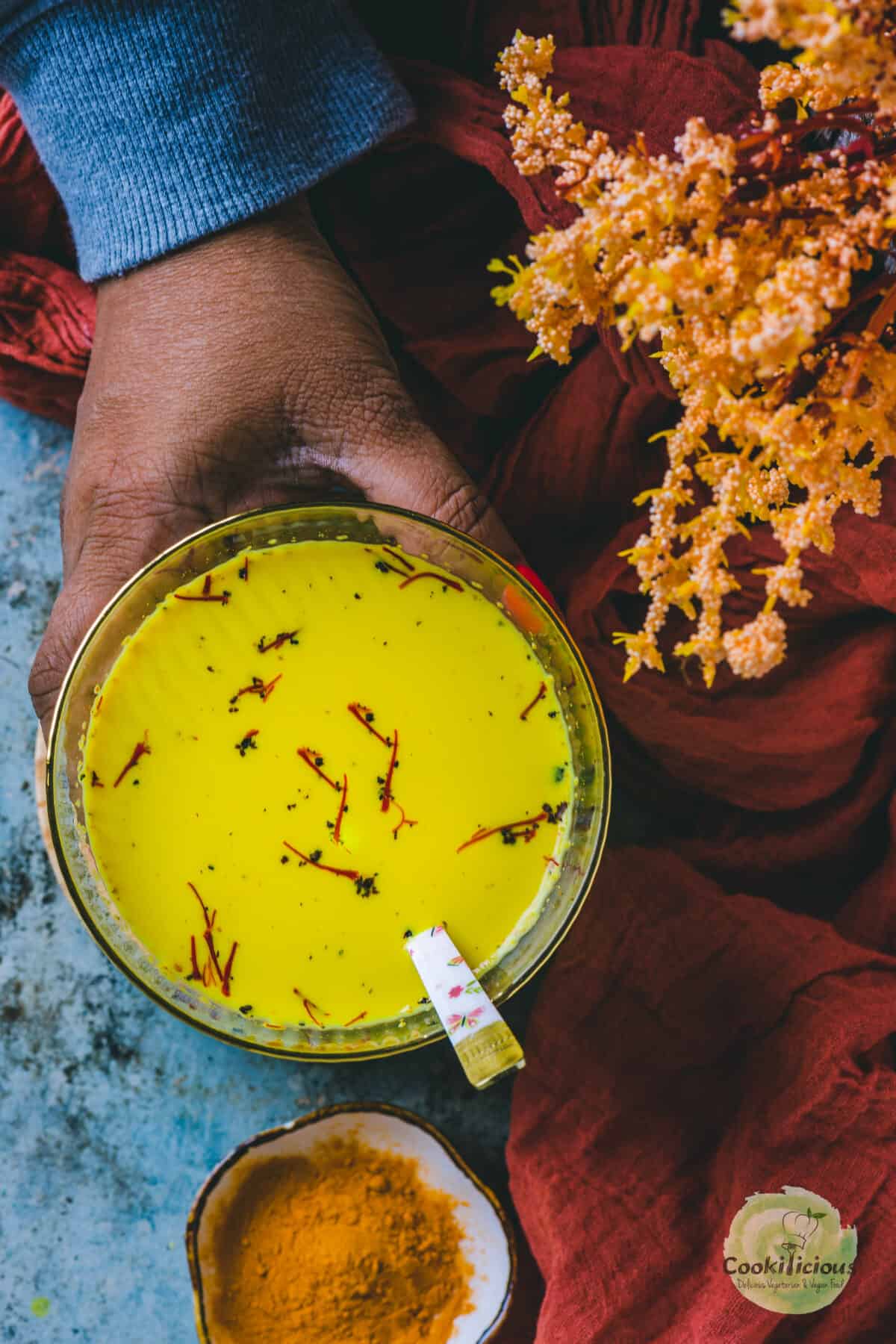 one hand holding a glass of haldi doodh with a spoon in it.