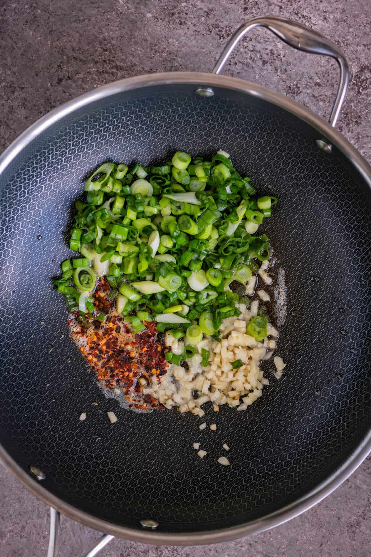 Garlic and scallions sautéing in sesame oil in a wok for vegan mushroom fried rice.