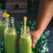 a hand reaching out to pick up a glass of cucumber chaas