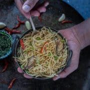 a set of hands holding a bowl of Chilly Garlic Noodles