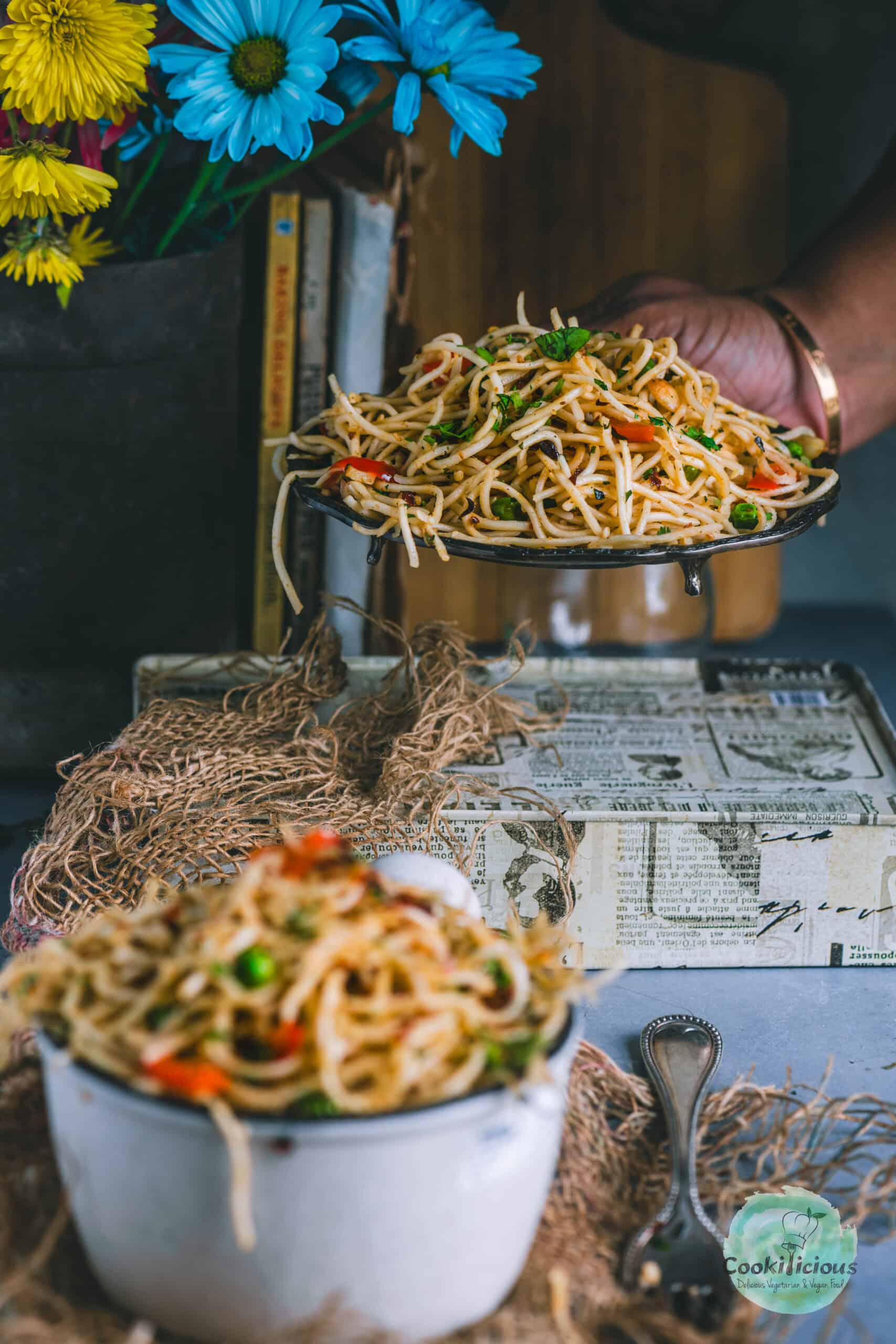 a hand picking up a bowl of Vegan Chili Garlic Noodles with another bowl of noodles in front of it.